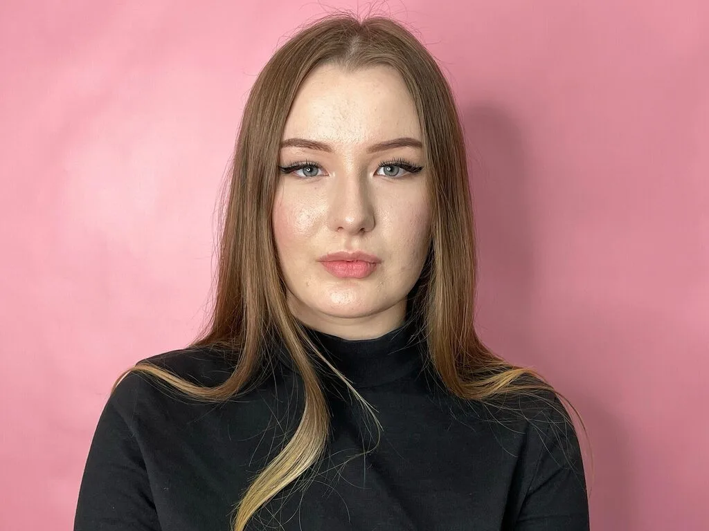 Sheba Browman poses in a black turtleneck against a pink background.