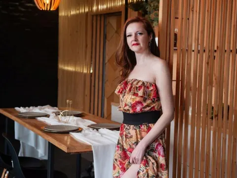 Megan Pirs — Megan Pirs stands in a floral strapless dress next to a dining table.