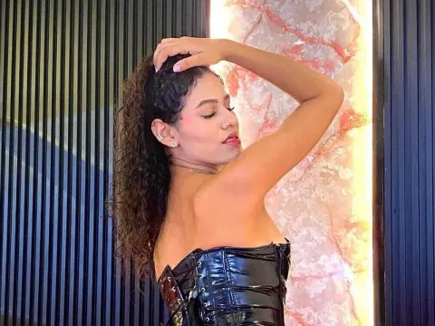 Hannah Jensen — Hannah Jensen poses with one arm raised, wearing a black shiny latex corset.