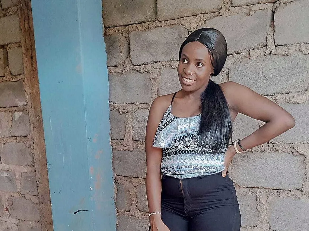 Princess Maria — Princess Maria poses outdoors in a patterned white tank top and black pants against a brick wall.