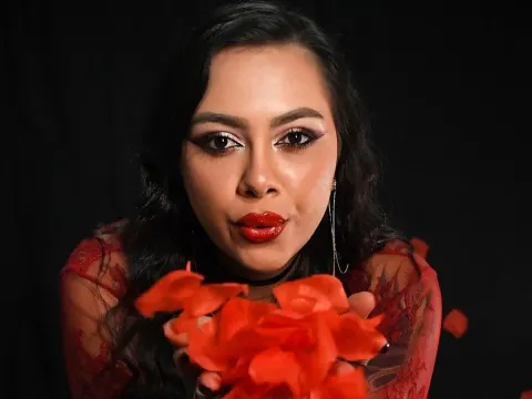Fenix Rose — Fenix Rose with long dark hair and red lipstick holds red flower petals in front of her face against a black background.
