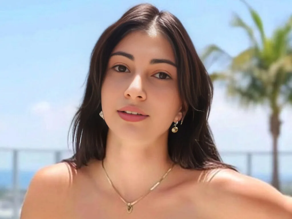 Pat Doogan looks at the camera wearing a gold necklace outdoors with palm trees in the background.