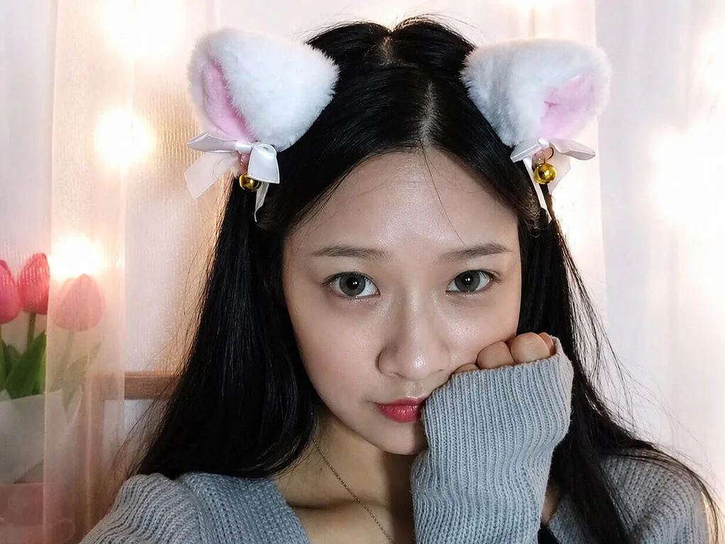Lily Pink Flower wears white bunny ears and a grey sweater while posing for a selfie.