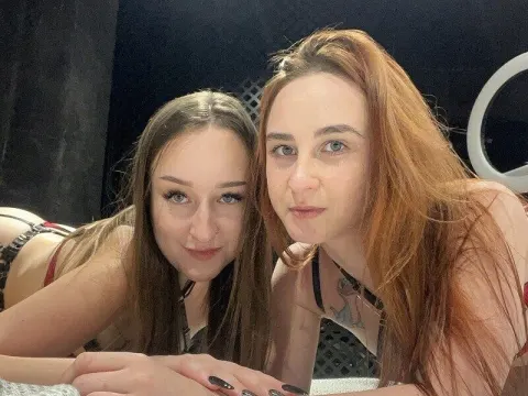 Sandra & Kathryn — Sandra & Kathryn lie close together on a bed, looking at the camera with long hair and dark tops.