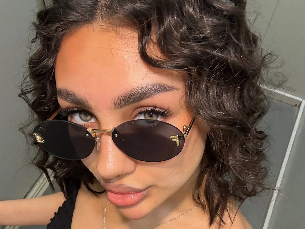 Earlene Gravlin wears dark sunglasses and a black top, looking directly at the camera with wavy dark hair.