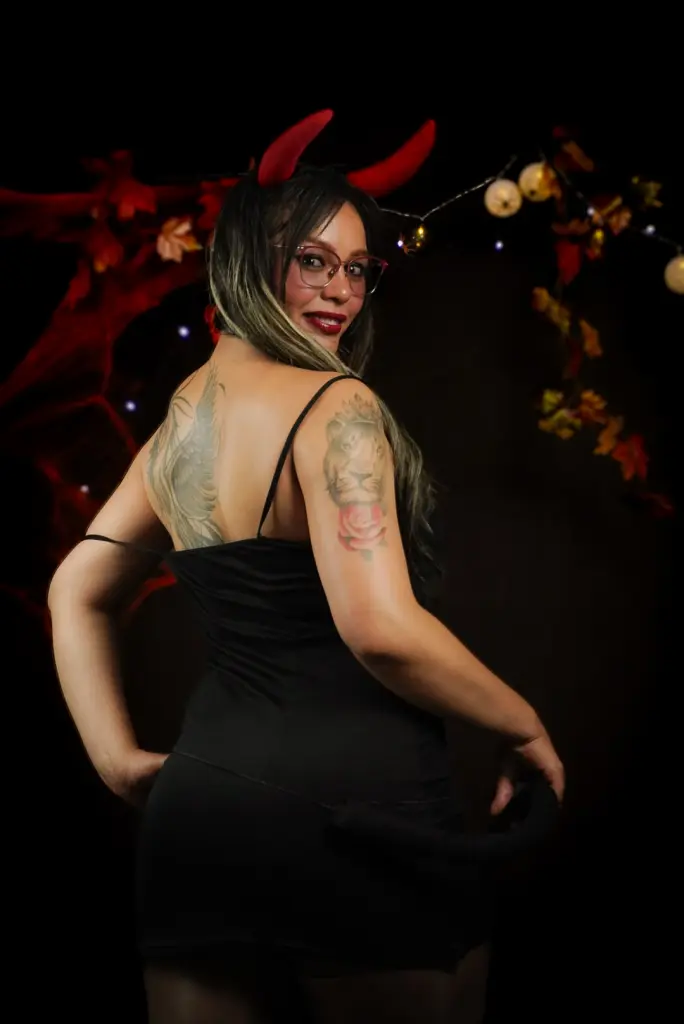 Confident woman in a blue bodysuit and glasses posing in a modern indoor setting.
