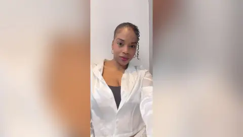 Smiling woman in a white blazer and black top posing in a bright indoor setting.