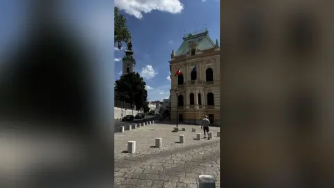 Man walking through a sunny historic European cobblestone plaza near a grand classical building.