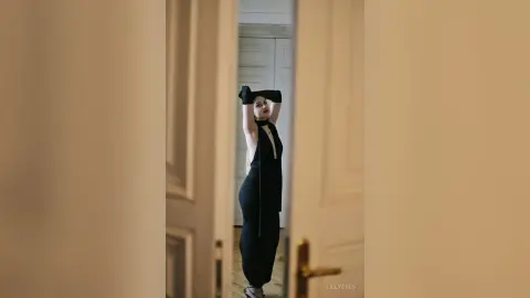 Elegant woman in a sleek black evening gown posing in a minimalist luxury interior with a sophisticated mood.