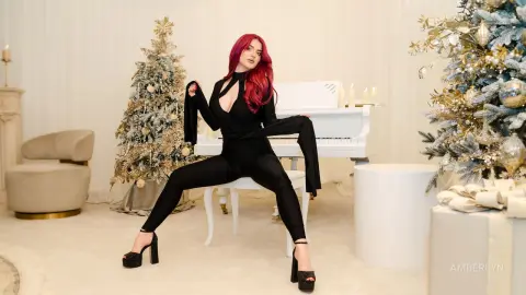 Elegant woman in a black jumpsuit posing by a white piano and decorated Christmas trees in a festive room.
