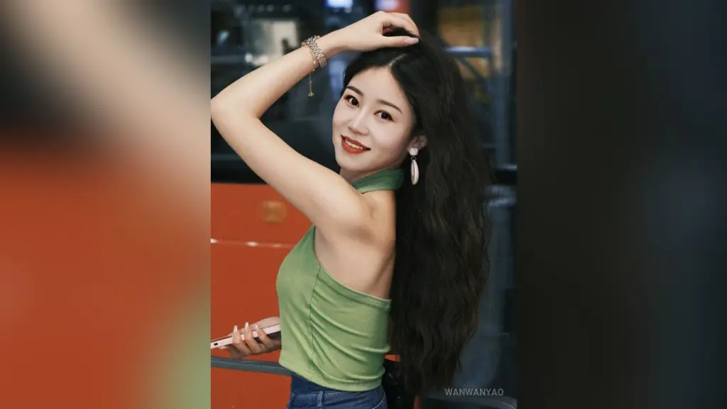 WanwanYao — Smiling young woman in a green tank top posing with long wavy hair in a modern indoor setting.