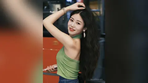 Smiling young woman in a green tank top posing with long wavy hair in a modern indoor setting.