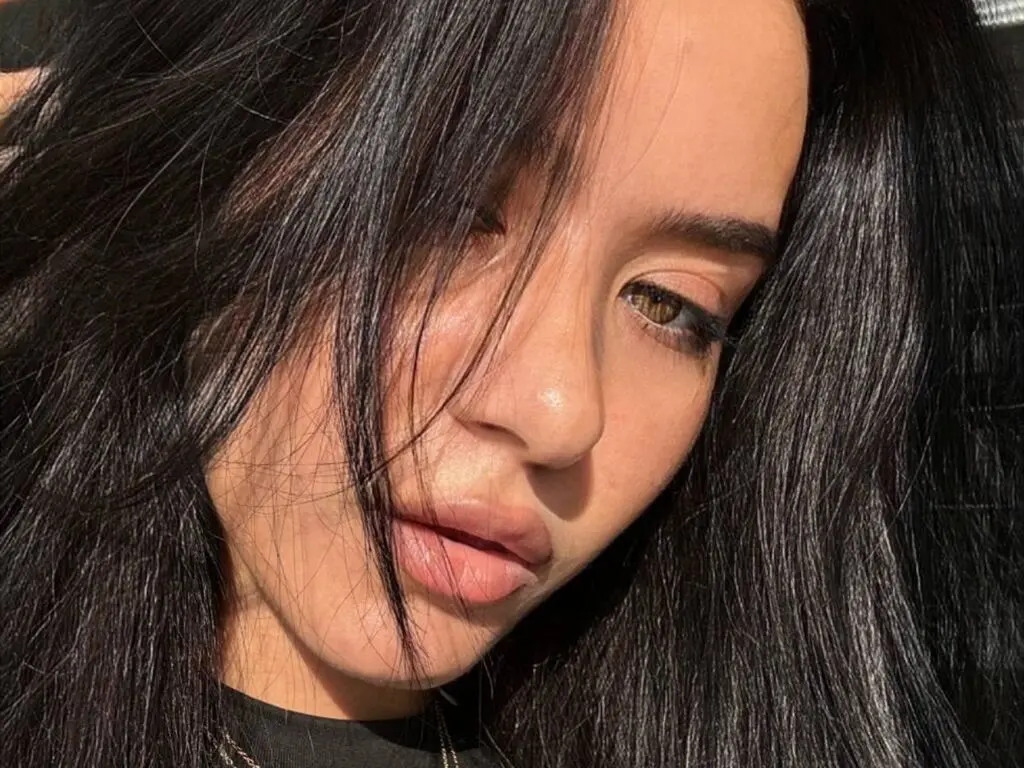 Close-up portrait of a woman with long dark hair and natural makeup in warm sunlight.