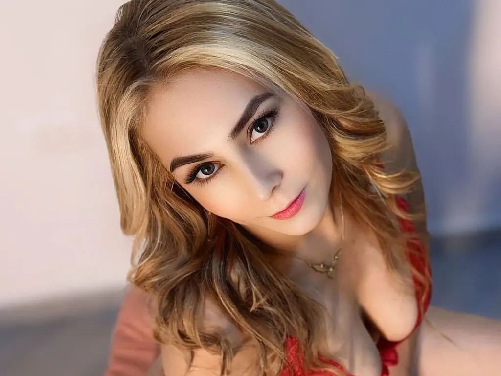 GiselaBell poses with long blonde hair, wearing a red lace top that shows off her cleavage.