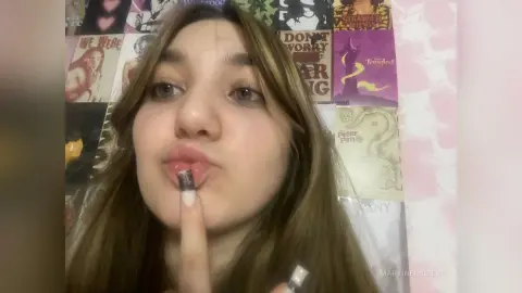 MartineKibbey pouts her lips while holding a finger to her mouth, showing her long brown hair against a background of movie posters.
