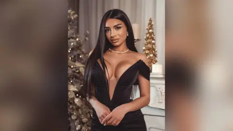 Glamorous woman in a sleek black plunging evening gown posing elegantly in a festive holiday setting.