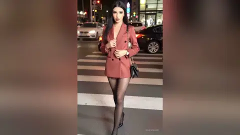 Stylish woman in a terracotta blazer and black tights walking on a city street at night.