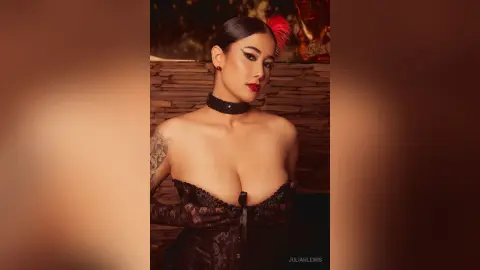 JuliahLewis poses in black lace lingerie and a black choker, showing her cleavage and shoulder tattoo against a textured wall.