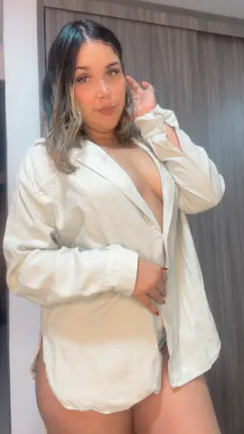 Curvy woman in an oversized white button-down shirt posing in a cozy indoor setting with a relaxed mood.