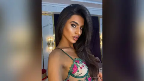 Glamorous woman in a floral lace corset top posing in a luxury hotel room with warm lighting.