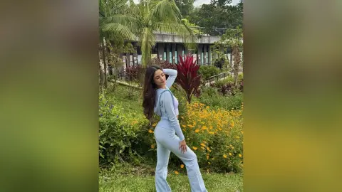 TefyRusso poses outdoors in a garden, wearing a light blue long-sleeve crop top and matching flared pants with her hair down.