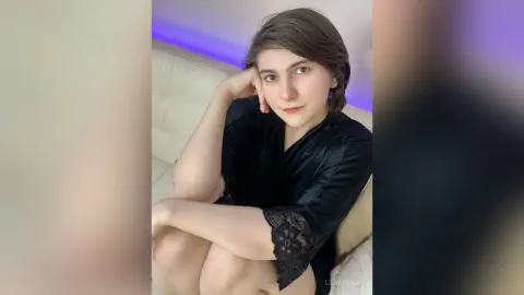 Young woman in a black satin robe relaxing on a white sofa in a moody, dimly lit room.