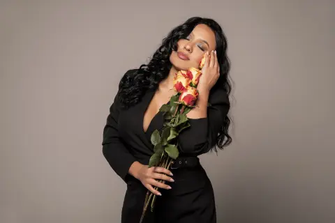 Elegant woman in a black dress holding orange roses against a neutral background with a romantic mood.