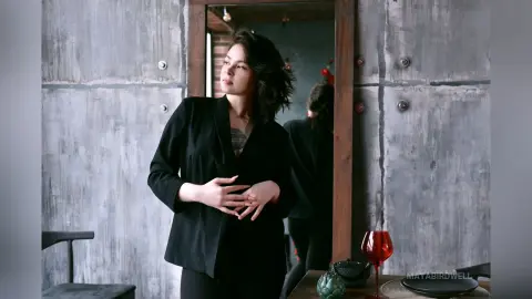 Elegant woman in a black blazer standing in a rustic industrial loft with a moody, sophisticated atmosphere.