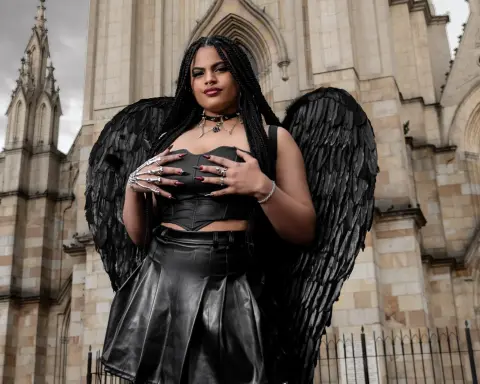 Gothic woman in black leather outfit and large feathered wings posing in front of a stone cathedral.