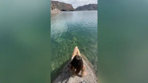 Young woman in casual summer wear sitting on a rock by a serene turquoise mountain lake.