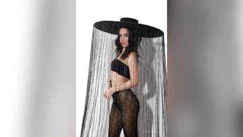 Elegant woman in a black strapless top and sheer patterned tights wearing a wide-brimmed hat with silver fringe.