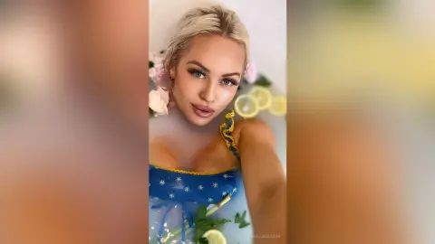Blonde woman in a blue floral swimsuit relaxing in a milky bath with lemon slices and flowers.