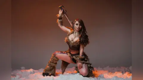 Cosplayer in a primal fur outfit kneeling in snow holding a fantasy sword with a fierce mood.