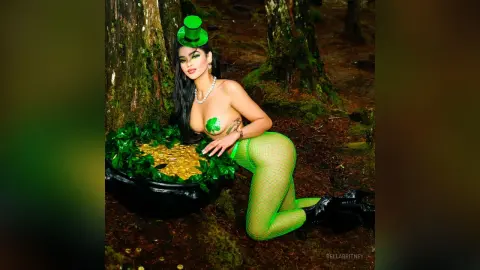Woman in green leotard and top hat sitting by a pot of gold in a magical forest setting.