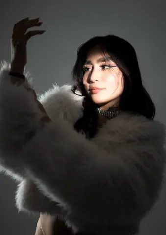 Elegant woman in a white faux fur coat and silver necklace posing with dramatic studio lighting.