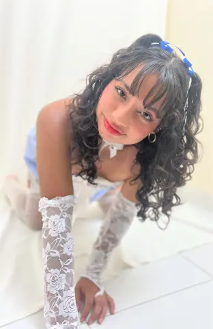 Young woman with curly hair wearing white lace gloves and a blue dress in a bright, dreamy setting.
