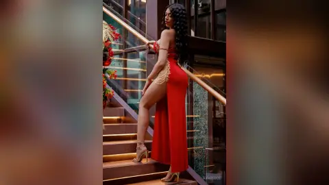 Elegant woman in a long red slit dress posing on modern stairs for a glamorous evening look.