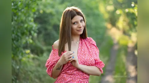 MarryMenedez smiles while posing outdoors in a pink floral dress with her hair down.