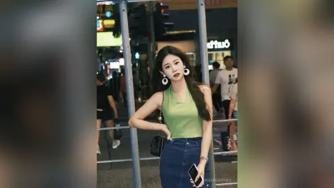 Young woman in a green halter top and denim jeans posing on a city street at night.