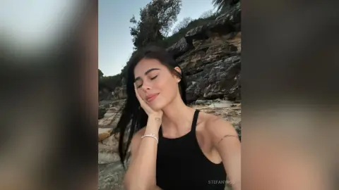 Young woman in a black tank top relaxing peacefully against a rocky cliffside landscape at dusk.