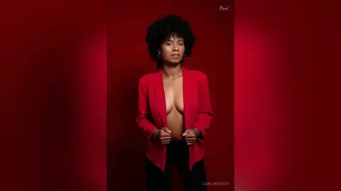 Confident woman in a red blazer and black trousers posing against a deep red studio background.