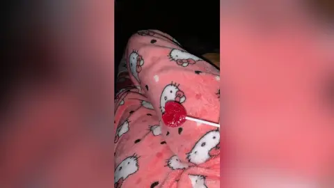 Cozy pink Hello Kitty patterned fleece pajamas and a red heart lollipop in a soft, comfortable setting.