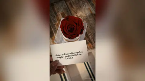KimRoberth holds a small white card with handwritten text next to a single large red rose in a clear container.