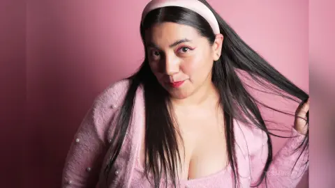 Smiling woman in a pink fuzzy cardigan and headband posing against a soft pink background.