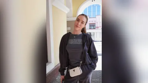 AmiliRay — AmiliRay stands outdoors in a dark grey tracksuit and a black zip-up hoodie with a small white crossbody bag.