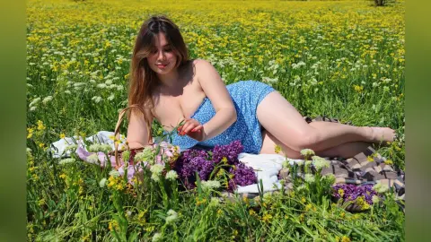 Young woman in a blue floral swimsuit relaxing on a picnic blanket in a sunny yellow wildflower field.