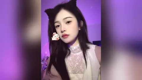 HedyIvy poses with long dark hair and cat ears, wearing a white lace top against a purple background.