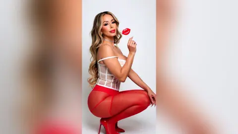 Glamorous woman in a white corset and red tights posing playfully against a white studio background.