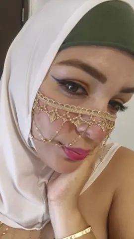 Woman in white hijab and ornate gold face jewelry posing with a serene expression indoors.