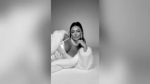 Glamorous woman in a white satin corset and faux fur coat posing elegantly in a black and white studio setting.